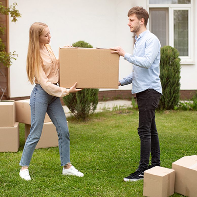 Young married couple carrying cardboard box in front of their new home on moving day Young married couple carrying cardboard box in front of their new house on moving day